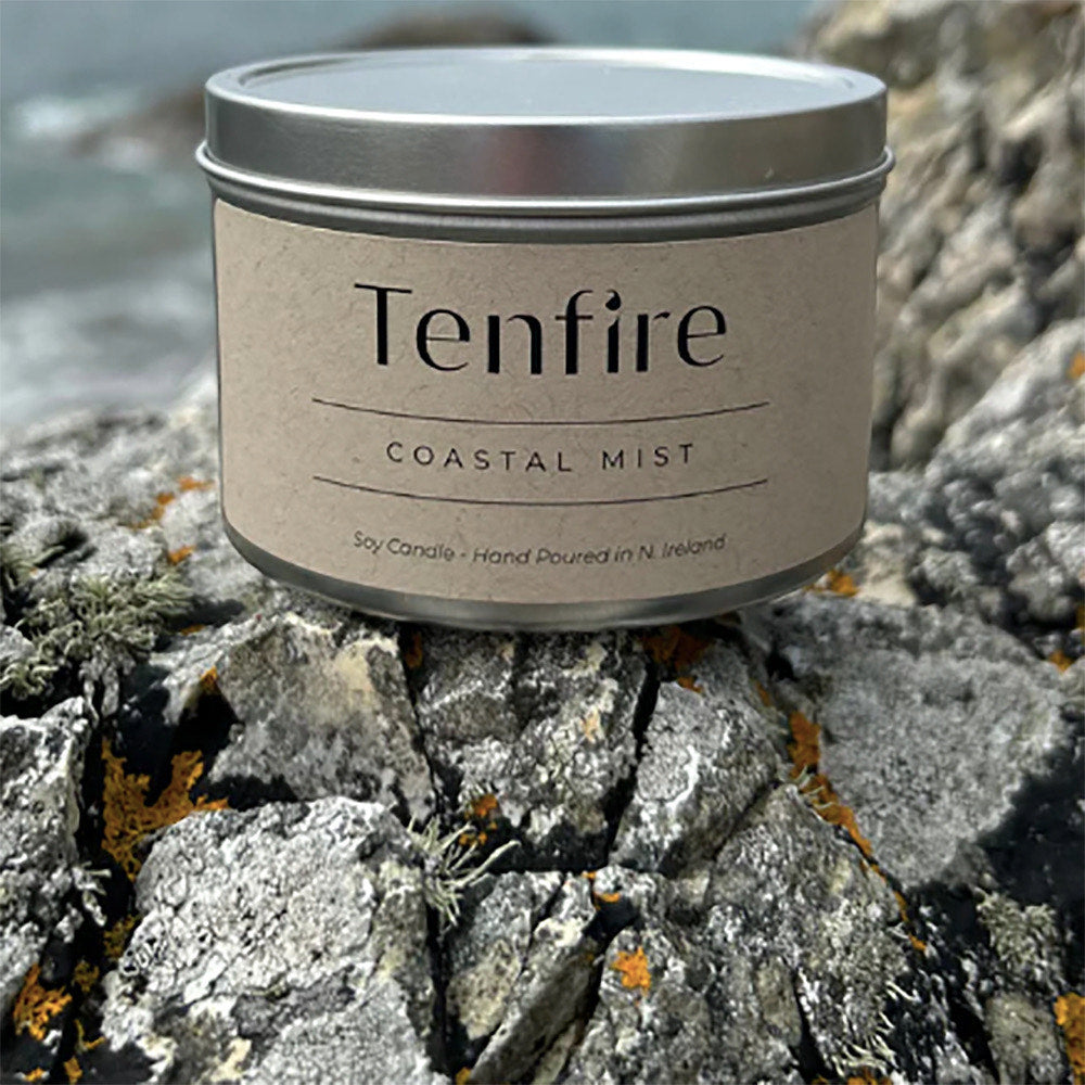 Candle tin labeled Tenfire Coastal Mist on a rock.