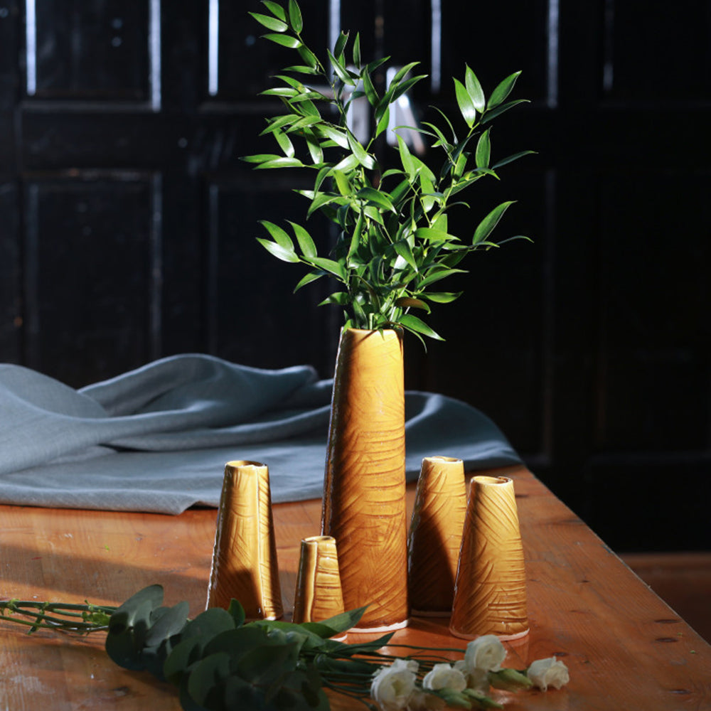 Mustard vase lifestyle still life with greenery and flowers.