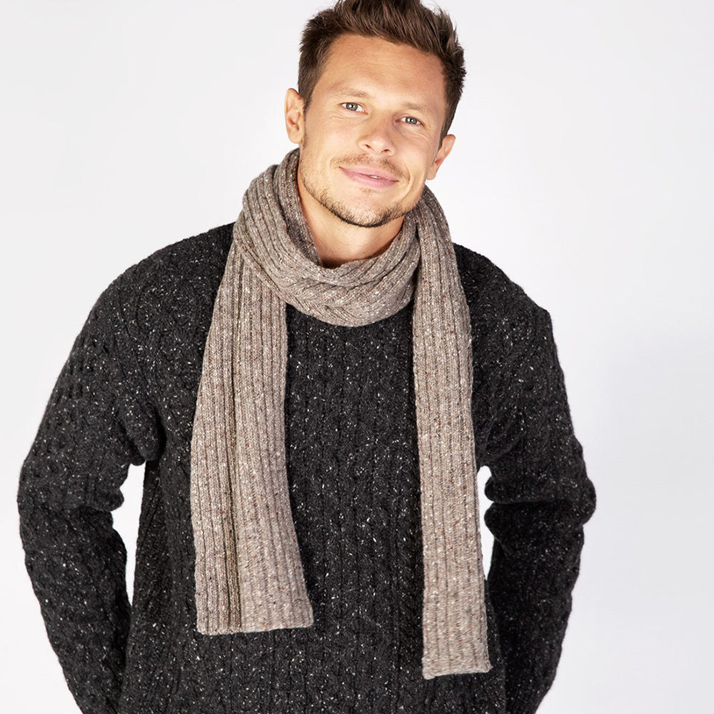 Man wearing a tan ribbed scarf on rocky ground.