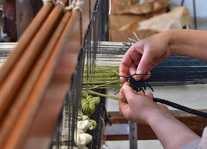 person weaving threads on a loom 