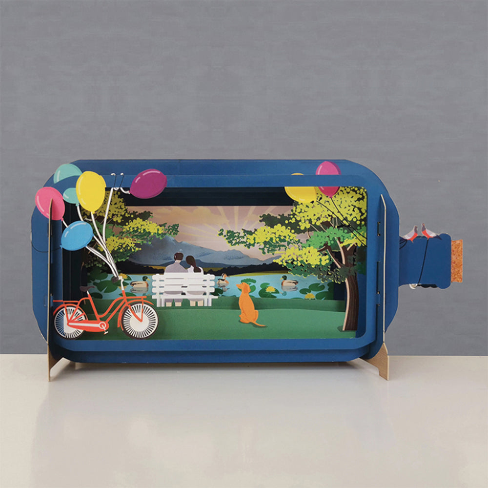 Couple on bench in message in a bottle art with balloons and bike.