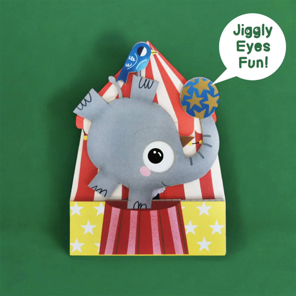 Elephant with jiggly eyes balancing ball in circus.