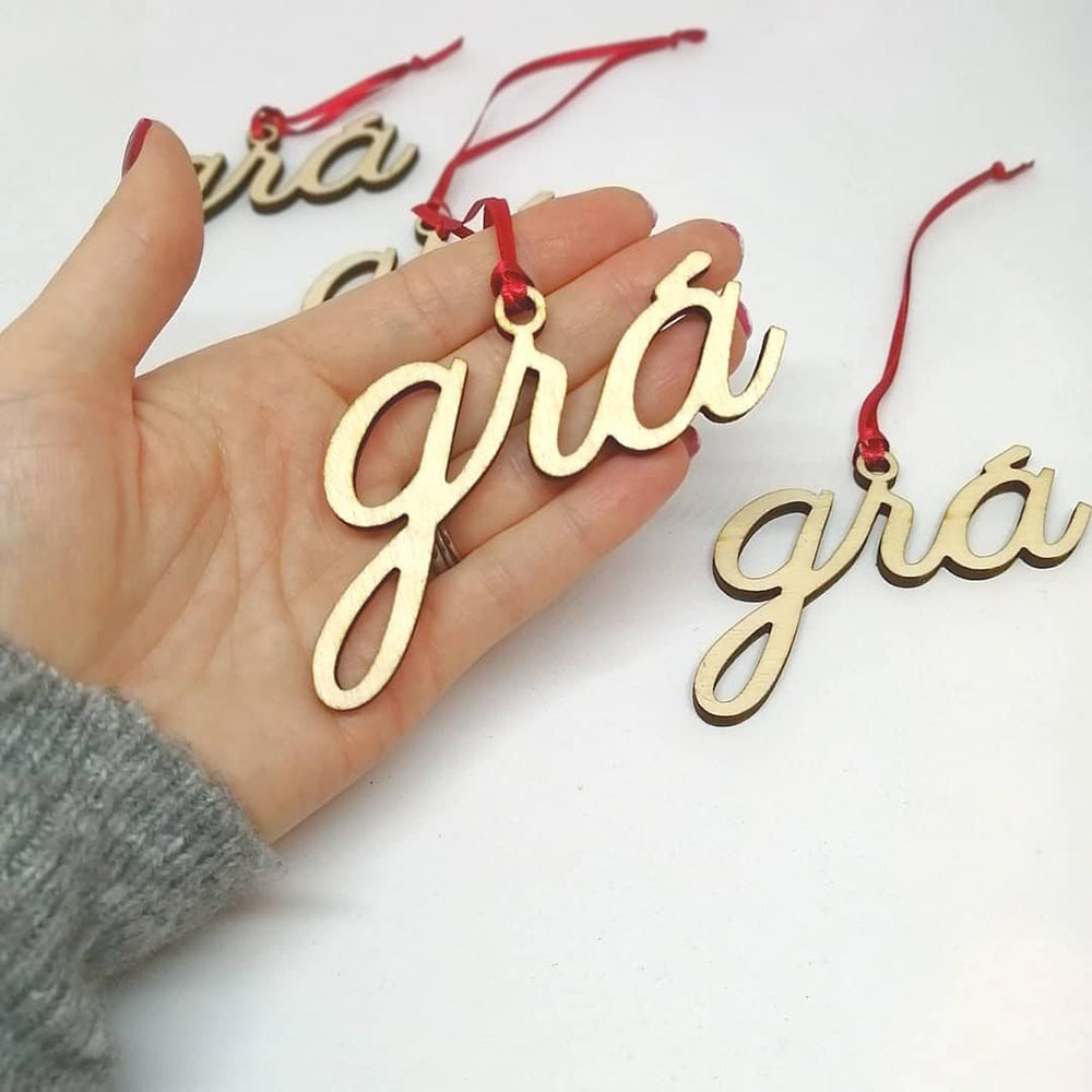 Wooden 'grá' Christmas ornament held in hand with red ribbon